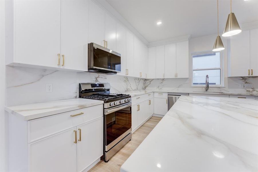 This stunning kitchen features gold hardware, quartz countertops, gas range, and stainless steel appliances. There is plenty of storage space in the cabinets.