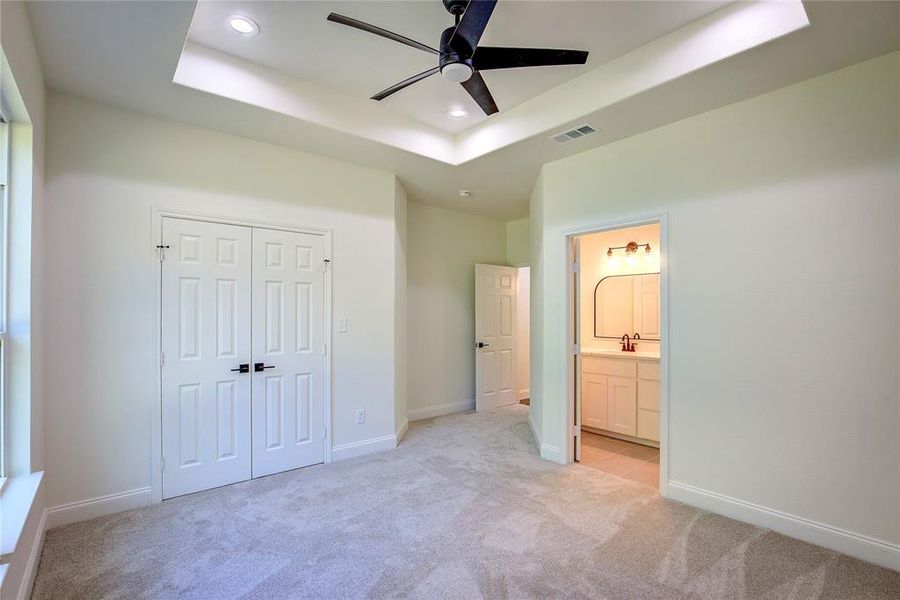 Unfurnished bedroom with a tray ceiling, light carpet, recessed lighting, a closet, and connected bathroom Unfurnished bedroom with a tray ceiling, light carpet, recessed lighting, a closet, and connected bathroom