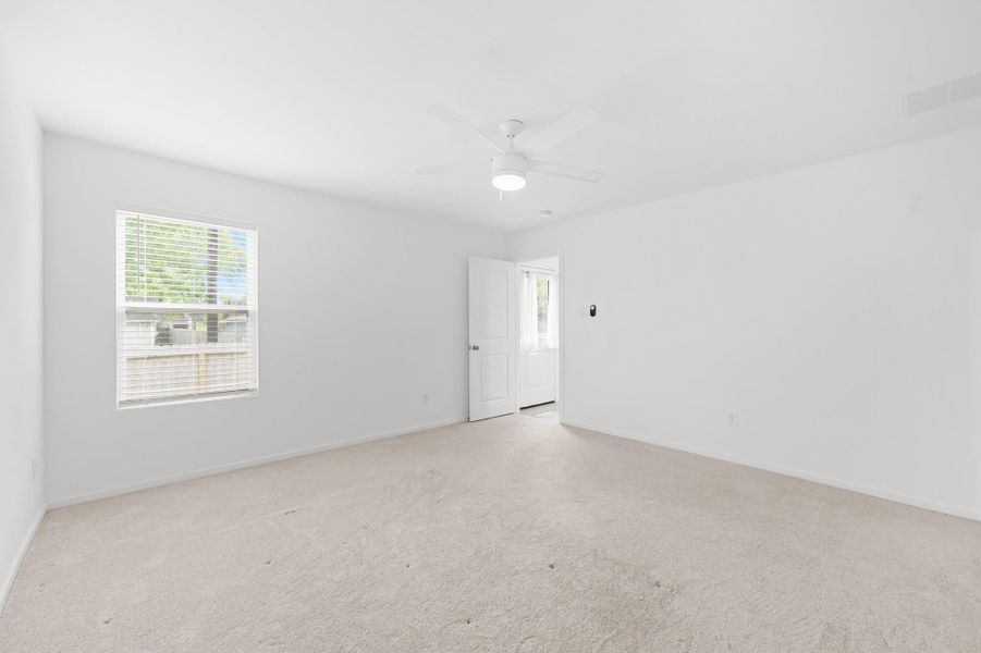 Spacious primary bedroom features neutral carpeting, a ceiling fan, and a large window that brings natural light into the room. Spacious primary bedroom features neutral carpeting, a ceiling fan, and a large window that brings natural light into the room.
