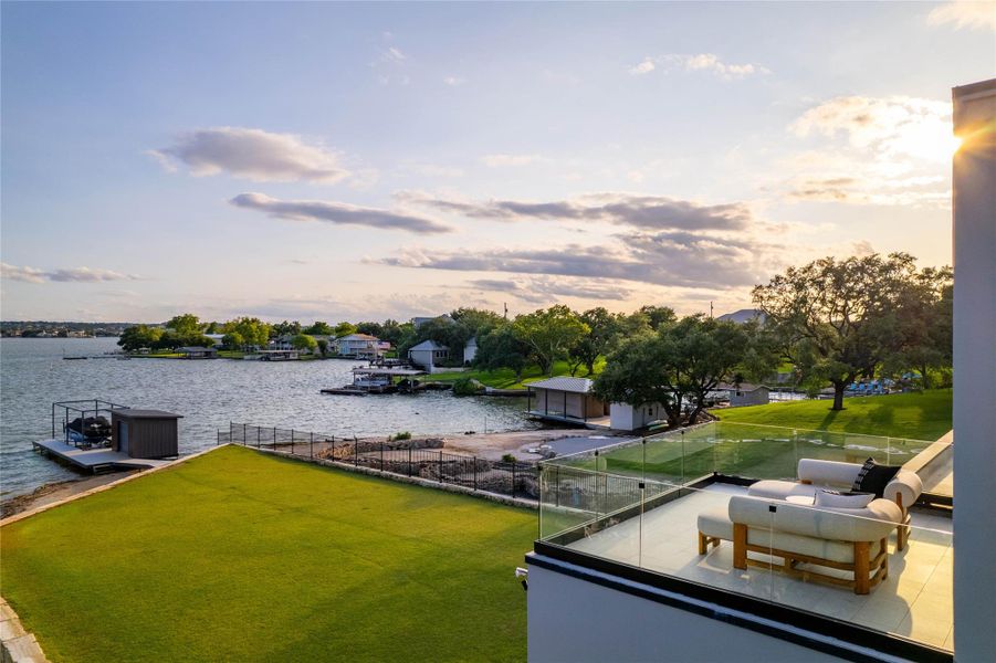Waterfront property featuring a private dock with covered boat lift, expansive artificial turf lawn, and a spacious tile-surfaced balcony with glass railing