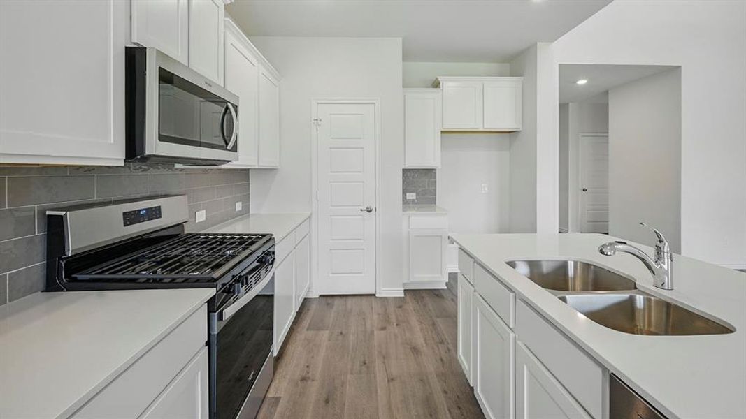 Modern kitchen featuring white cabinetry, light countertops, stainless steel appliances, a subway tile backsplash, and wood-finish flooring Modern kitchen featuring white cabinetry, light countertops, stainless steel appliances, a subway tile backsplash, and wood-finish flooring