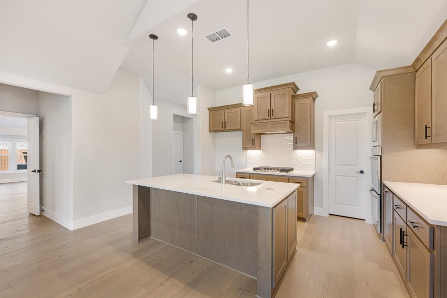 Kitchen with large center island, wood cabinets, white countertops, pendant lights, and light hardwood floors Kitchen with large center island, wood cabinets, white countertops, pendant lights, and light hardwood floors