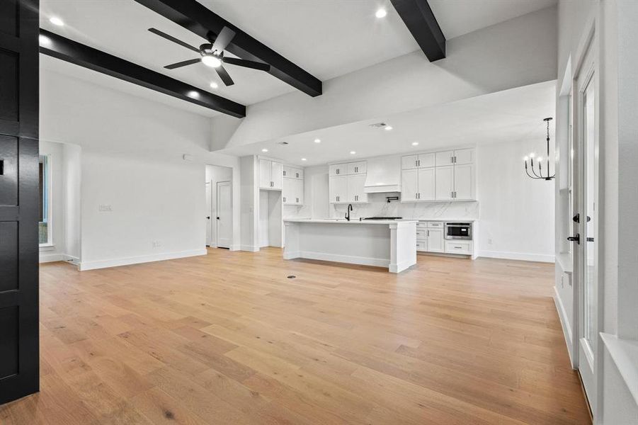 Unfurnished living room featuring recessed lighting, beam ceiling, light wood-style floors, a chandelier, and ceiling fan