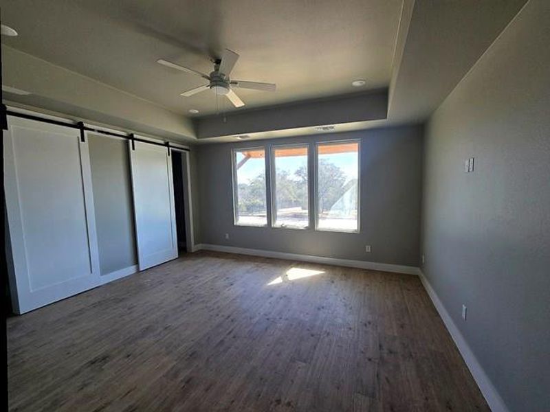 Unfurnished bedroom featuring a barn door, dark wood-style floors, a raised ceiling, and a ceiling fan