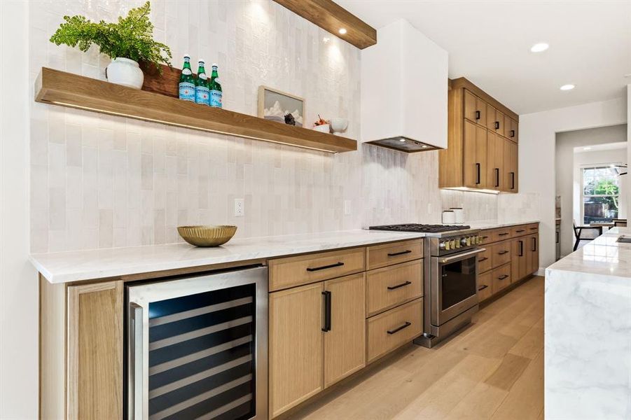 Kitchen with light stone counters, open shelves, beverage cooler, high end stainless steel range oven, and light wood-style flooring