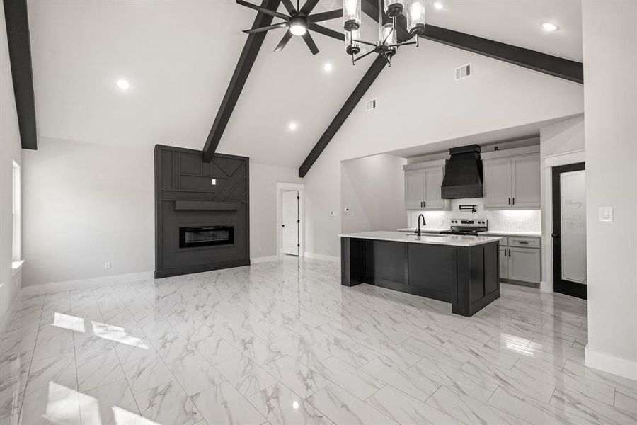 Dual tone kitchen featuring a kitchen island with sink, open floor plan, a large fireplace, recessed lighting, and light stone counters