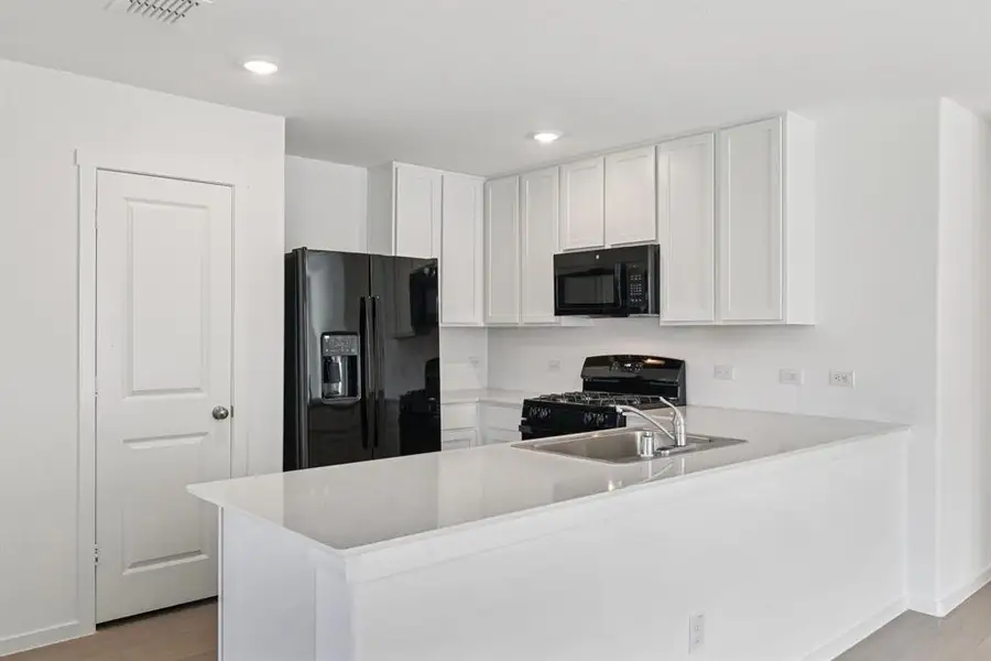 Kitchen featuring black appliances, a peninsula, light wood-style flooring, light countertops, and white cabinets