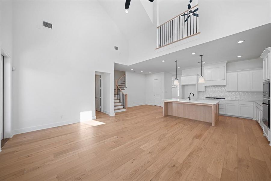 Kitchen with white cabinetry, open floor plan, a high ceiling, light wood finished floors, and recessed lighting