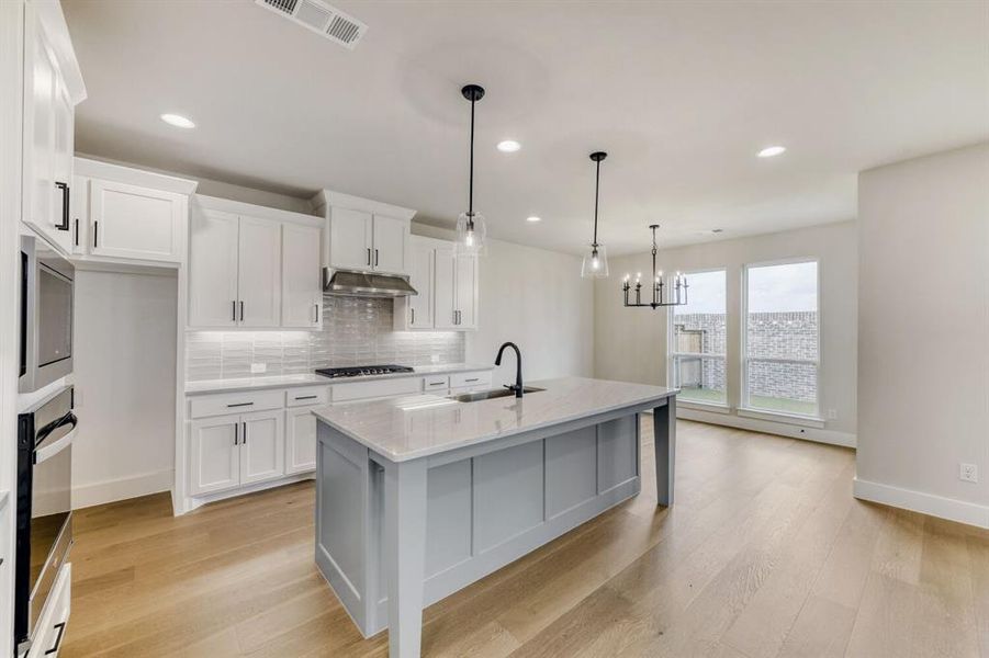Modern kitchen featuring white shaker cabinetry, light wood-finish flooring, a gray island with a countertop, stainless steel appliances, and a tiled backsplash
