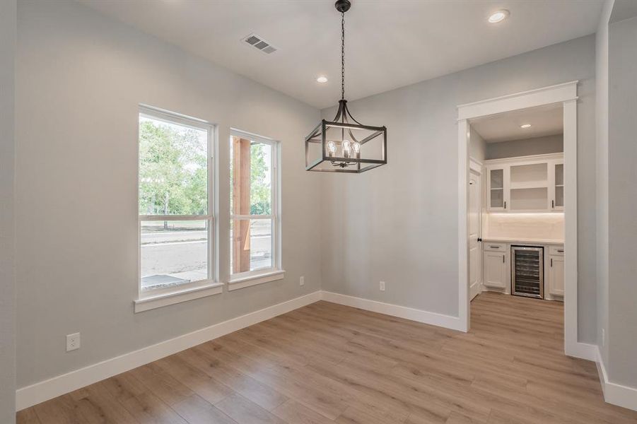 Unfurnished dining area with a notable chandelier, light wood-type flooring, and wine cooler