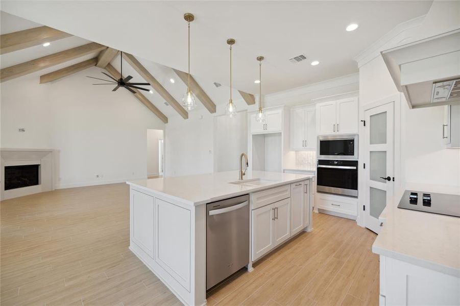 Kitchen featuring sink, an island with sink, white cabinetry, lofted ceiling with beams, and appliances with stainless steel finishes