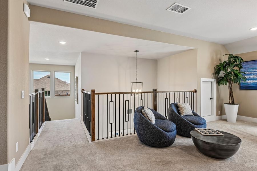 Upstairs loft area with iron stair railing, two blue accent chairs, and a pendant light fixture over carpet flooring Upstairs loft area with iron stair railing, two blue accent chairs, and a pendant light fixture over carpet flooring