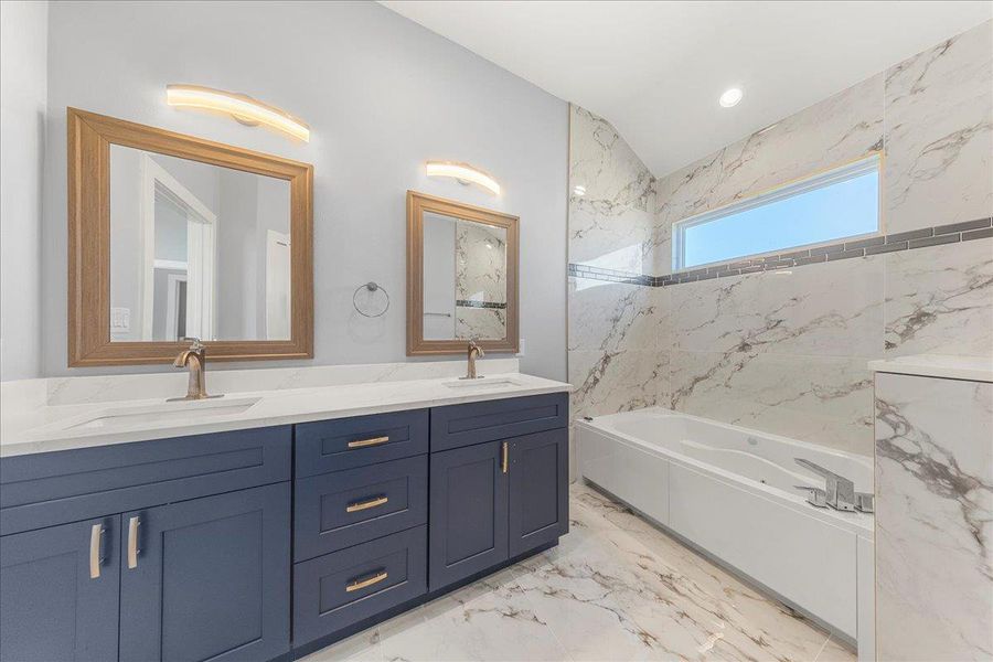 Full bath featuring double vanity, a tub with marble appearance, light marble finish floors, lofted ceiling, and recessed lighting Full bath featuring double vanity, a tub with marble appearance, light marble finish floors, lofted ceiling, and recessed lighting