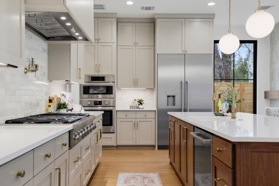 Kitchen with two tone color scheme, pendant lighting, light wood finished floors, light stone countertops, and stainless steel appliances