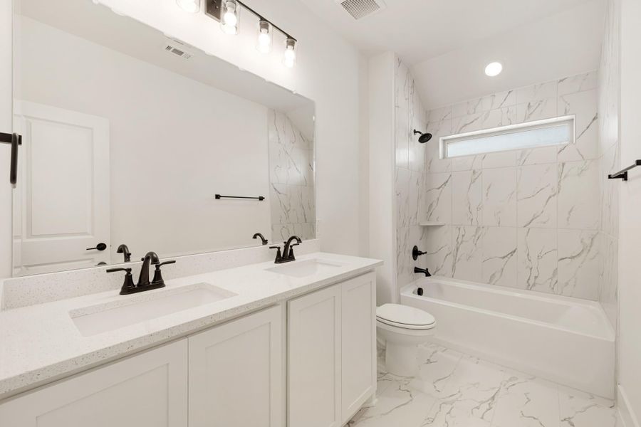 Bathroom with double vanity, white quartz countertop, marble tile tub surround, and dark bronze fixtures