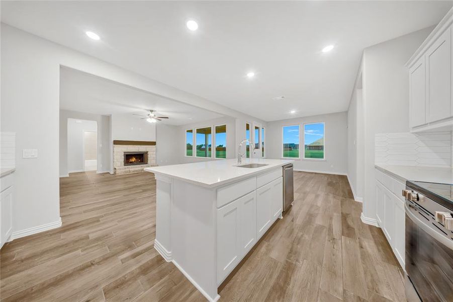 Kitchen with appliances with stainless steel finishes, a stone fireplace, white cabinets, light wood-type flooring, and recessed lighting Kitchen with appliances with stainless steel finishes, a stone fireplace, white cabinets, light wood-type flooring, and recessed lighting