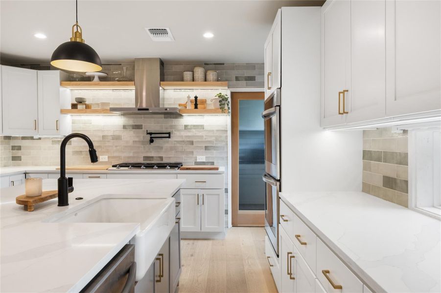 Kitchen featuring tasteful backsplash, light stone counters, island range hood, open shelves, and two tone color scheme