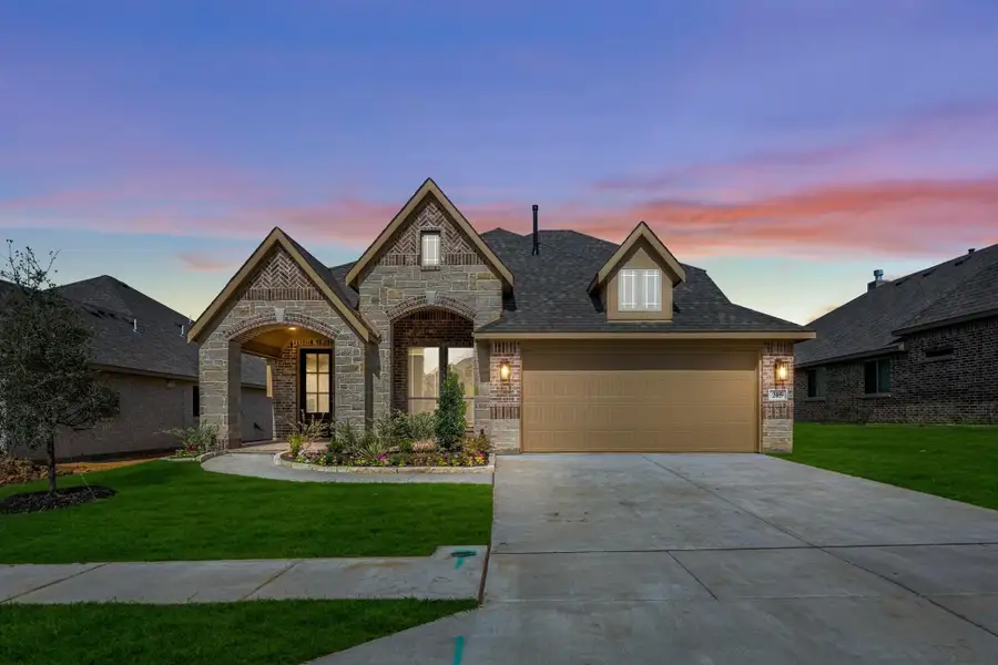 Single-story home with stone and brick exterior, two-car garage, and arched entryway at dusk