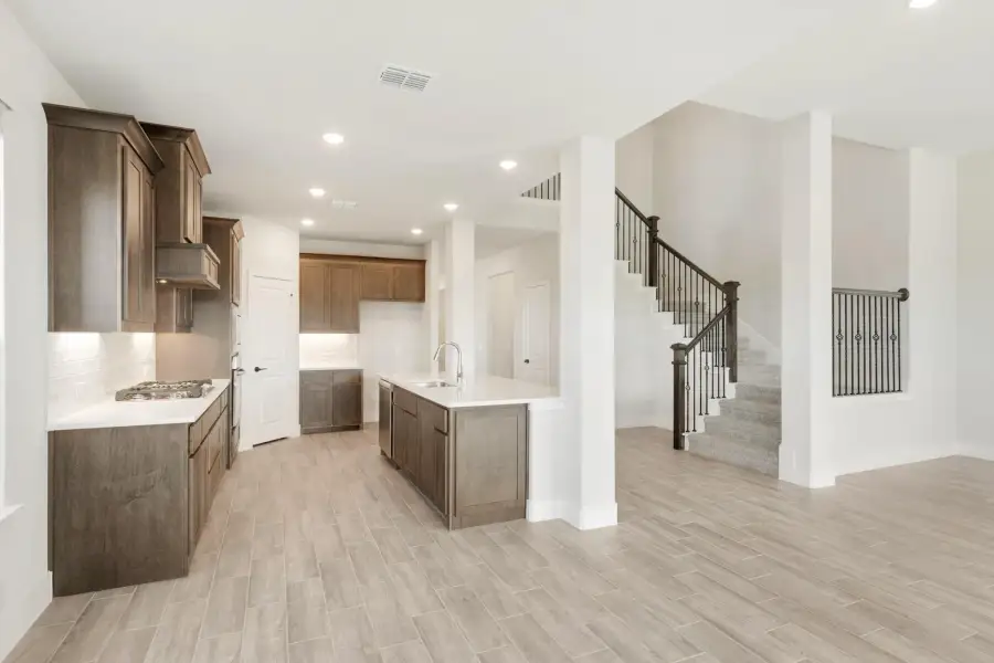 Open kitchen with dark wood cabinets, center island, and staircase visible in background