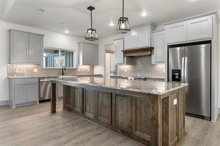 Two tone kitchen with stainless steel appliances, a center island, light stone counters, pendant lighting, and light wood-style flooring