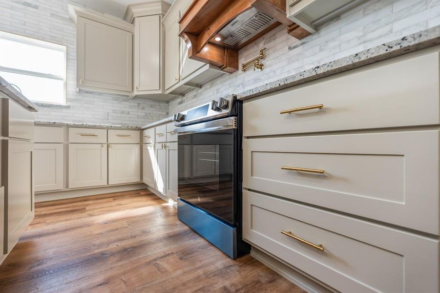 Kitchen featuring light wood-style flooring, tasteful backsplash, light stone counters, and beige cabinetry Kitchen featuring light wood-style flooring, tasteful backsplash, light stone counters, and beige cabinetry