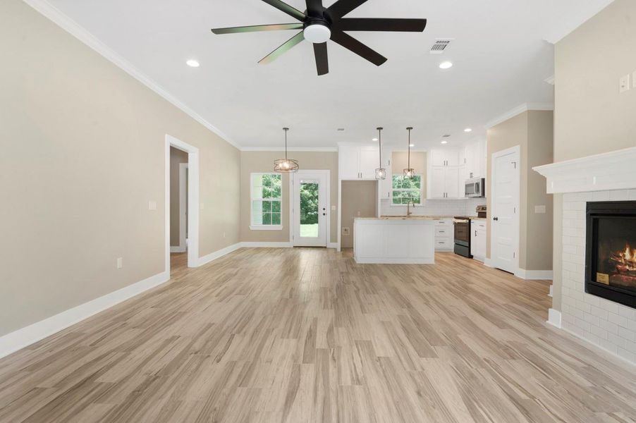 This spacious open-concept living area features modern wood flooring, a cozy fireplace, and a ceiling fan. The kitchen boasts sleek white cabinetry, stainless steel appliances, and an island with pendant lighting. Large windows provide ample natural light, enhancing the room's inviting atmosphere. This spacious open-concept living area features modern wood flooring, a cozy fireplace, and a ceiling fan. The kitchen boasts sleek white cabinetry, stainless steel appliances, and an island with pendant lighting. Large windows provide ample natural light, enhancing the room's inviting atmosphere.