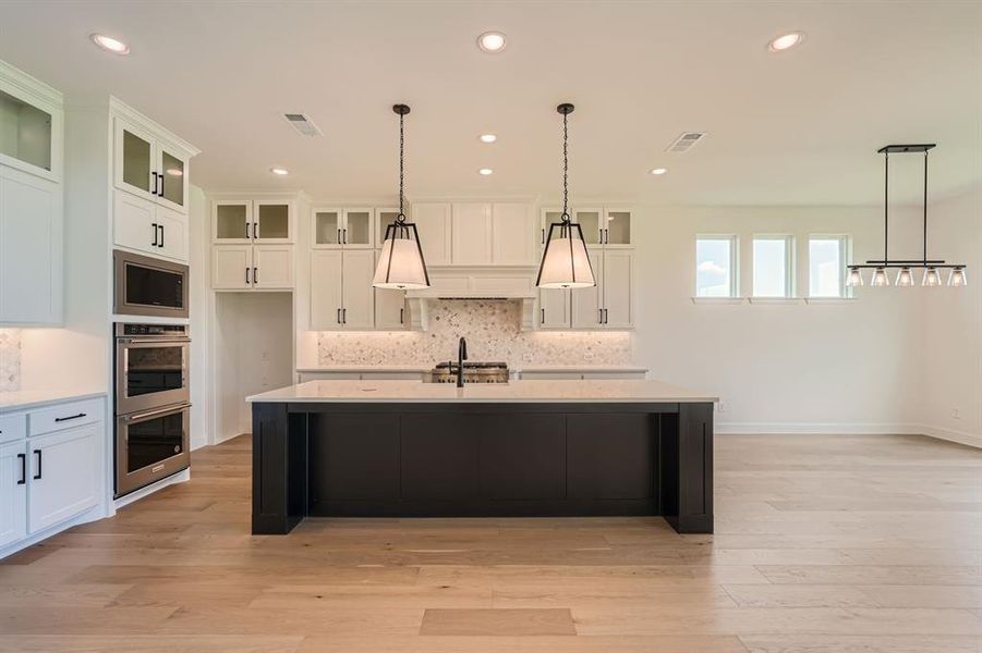 Kitchen featuring white cabinets, stainless steel appliances, light hardwood / wood-style flooring, and pendant lighting