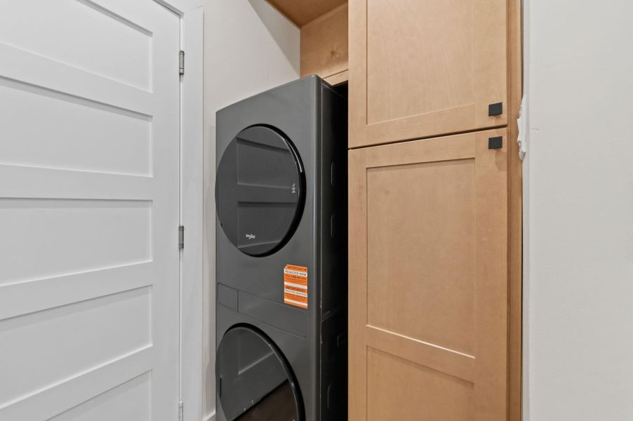 Modern laundry area featuring a sleek, stacked washer and dryer set adjacent to stylish wooden cabinetry for convenient storage.