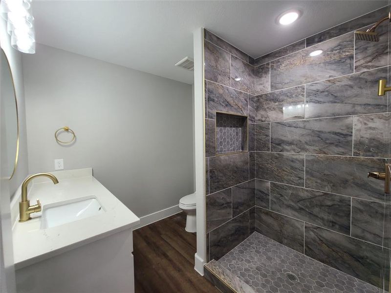 Bathroom with hardwood / wood-style flooring, vanity, a tile shower, and toilet