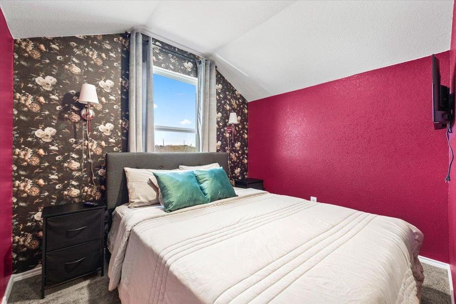 Carpeted bedroom featuring a textured wall and vaulted ceiling Carpeted bedroom featuring a textured wall and vaulted ceiling