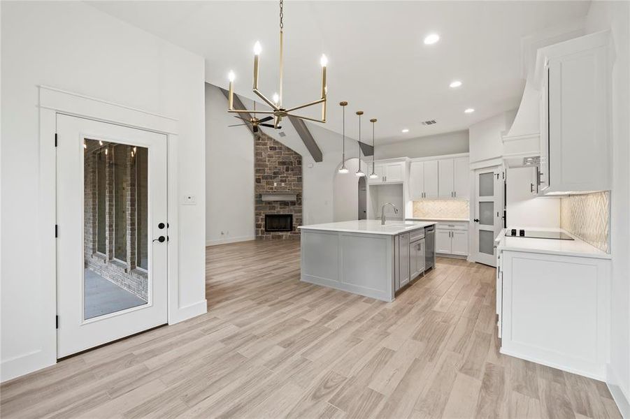 Kitchen with a chandelier, open floor plan, a stone fireplace, white cabinets, and decorative light fixtures