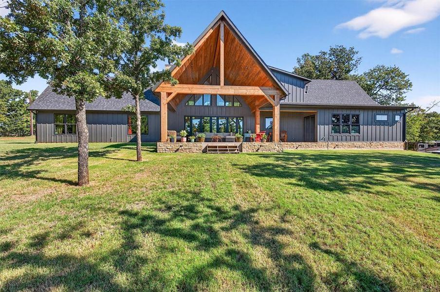 Rear view of house with a patio area, board and batten siding, a yard, and a shingled roof Rear view of house with a patio area, board and batten siding, a yard, and a shingled roof