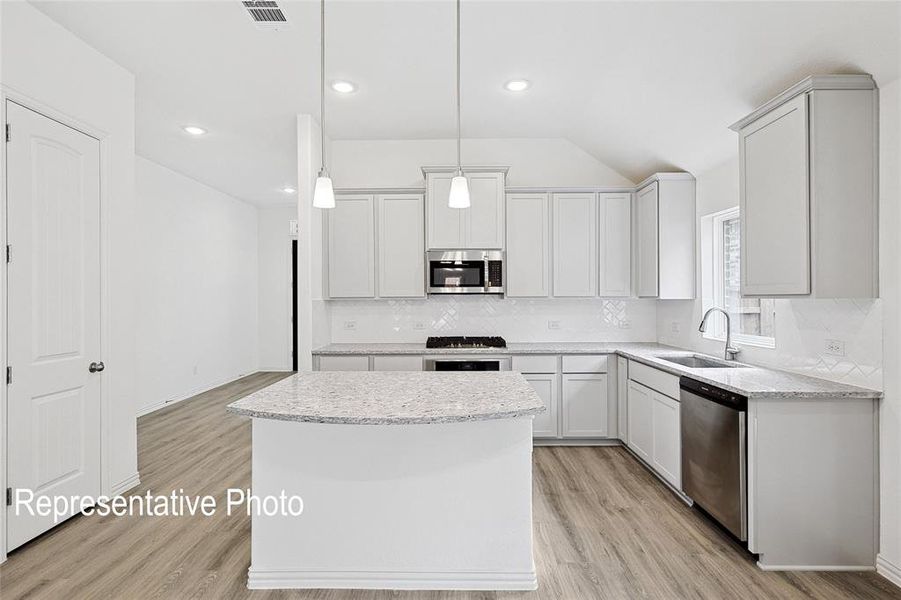 Contemporary kitchen featuring an island with stone countertop, light-toned cabinetry, stainless steel appliances, and wood-finish flooring