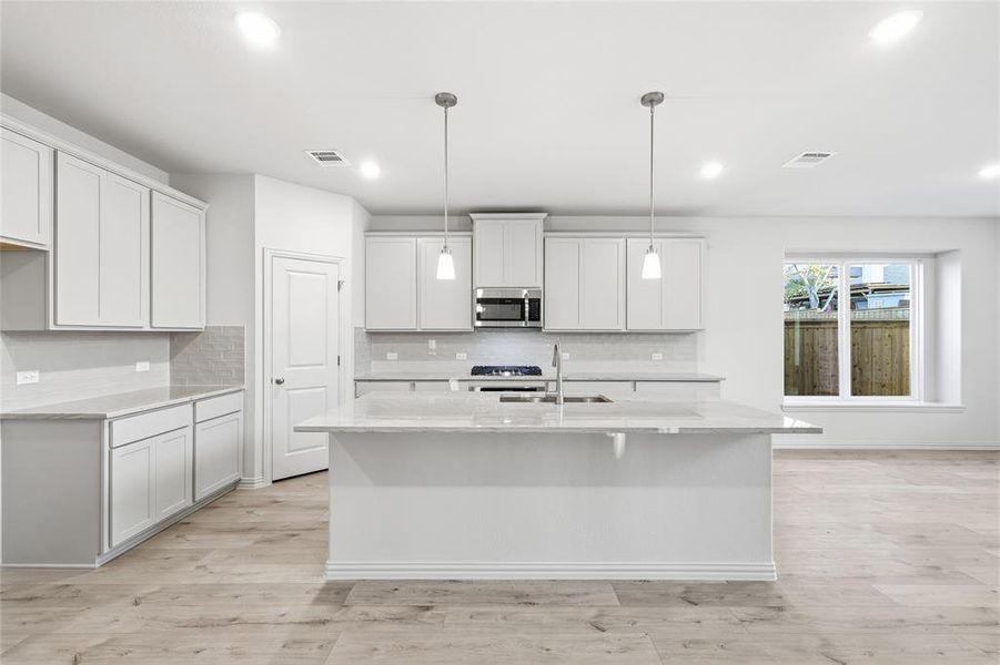 Kitchen with light stone countertops, hanging light fixtures, a kitchen island with sink, white cabinets, and recessed lighting
