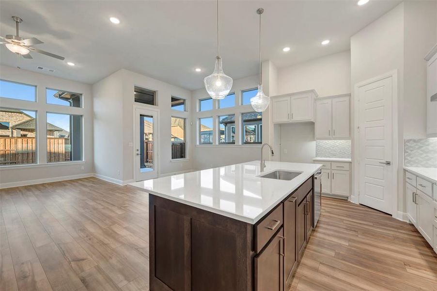 Two tone kitchen featuring two tone cabinetry, decorative backsplash, a center island with sink, light stone counters, and light wood-type flooring
