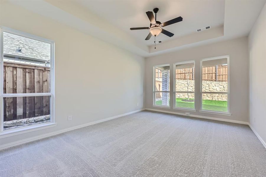 Carpeted spare room featuring ceiling fan and a tray ceiling