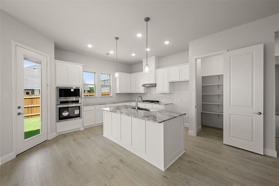 Kitchen with under cabinet range hood, tasteful backsplash, light stone countertops, white cabinets, and an island with sink Kitchen with under cabinet range hood, tasteful backsplash, light stone countertops, white cabinets, and an island with sink