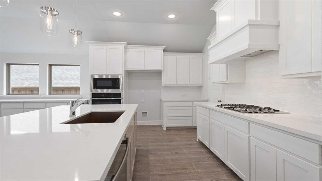 Kitchen featuring wood-type flooring, sink, white cabinetry, hanging light fixtures, and stainless steel appliances