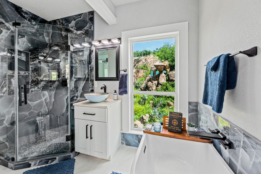 Bathroom featuring a glass-enclosed shower with dark-toned tile, a white vanity with a vessel sink, a white soaking tub, and a window with a natural landscape