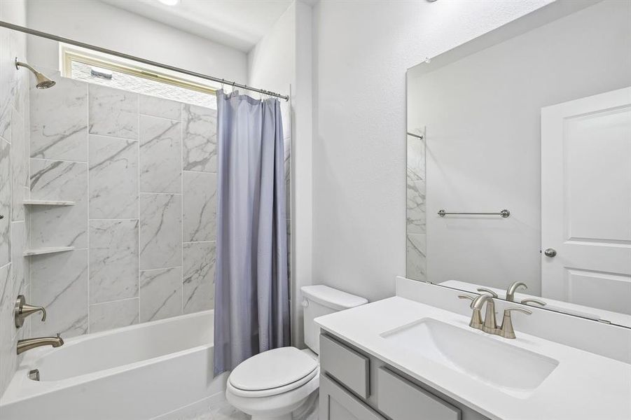 Full bathroom featuring a white tub with white-and-gray marbled tile surround, built-in shelving, and a window for natural illumination Full bathroom featuring a white tub with white-and-gray marbled tile surround, built-in shelving, and a window for natural illumination