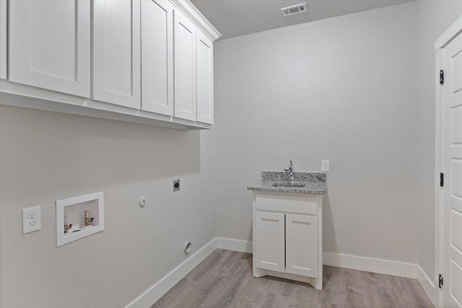 Clothes washing area with light hardwood / wood-style floors, cabinets, electric dryer hookup, sink, and hookup for a gas dryer