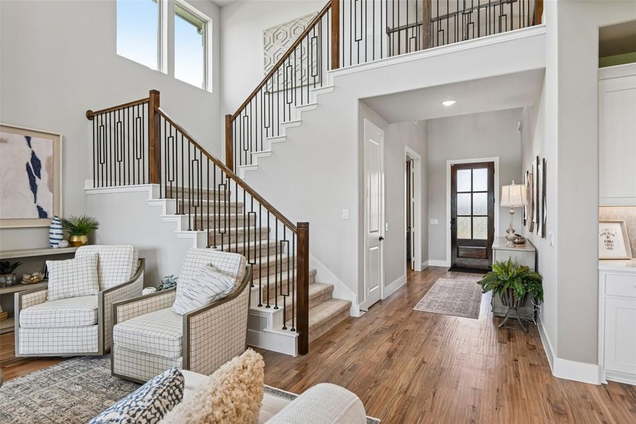 Two-story foyer with wood and iron staircase, hardwood floors, and front entry door visible down hallway Two-story foyer with wood and iron staircase, hardwood floors, and front entry door visible down hallway
