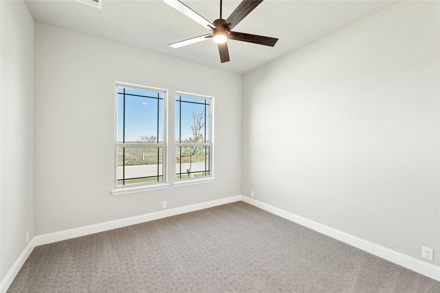 Empty bedroom with carpet flooring, ceiling fan, and two windows with outdoor views Empty bedroom with carpet flooring, ceiling fan, and two windows with outdoor views