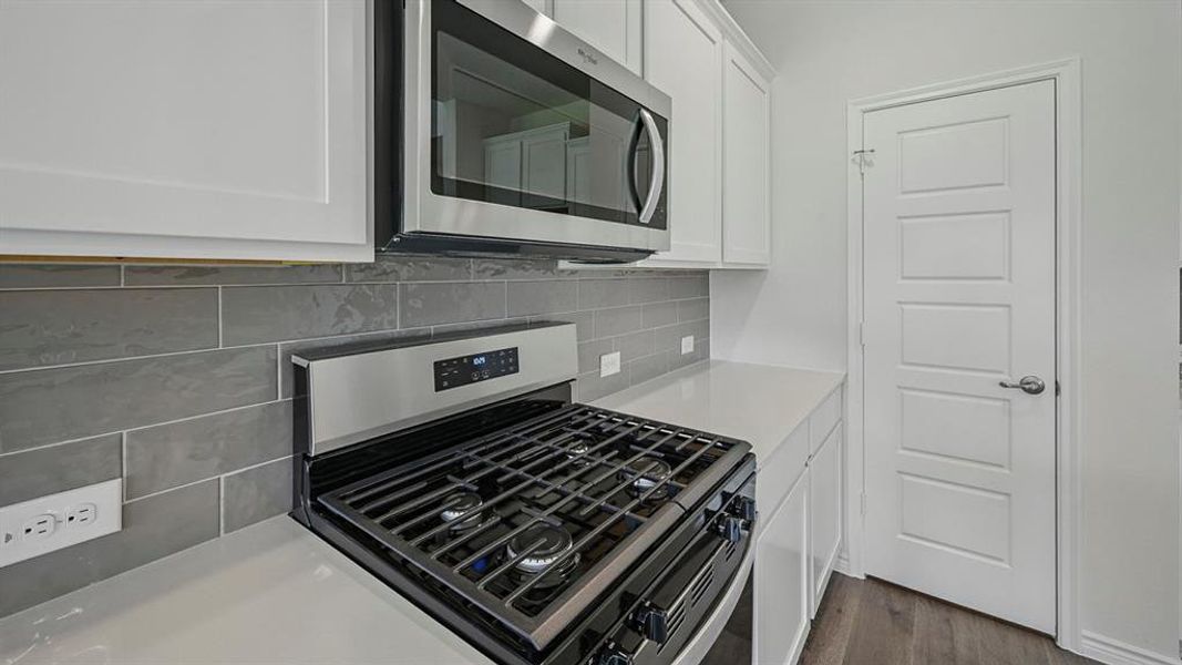 Kitchen featuring stainless steel gas range, coordinating microwave, white upper and lower cabinetry, light-toned countertops, and a gray subway tile backsplash Kitchen featuring stainless steel gas range, coordinating microwave, white upper and lower cabinetry, light-toned countertops, and a gray subway tile backsplash