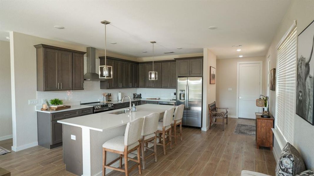 Kitchen with appliances with stainless steel finishes, a breakfast bar, dark brown cabinets, a kitchen island with sink, and wall chimney range hood