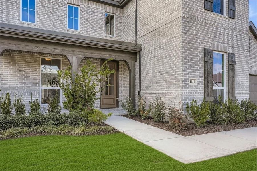 Doorway to property featuring brick siding, covered porch, and a lawn