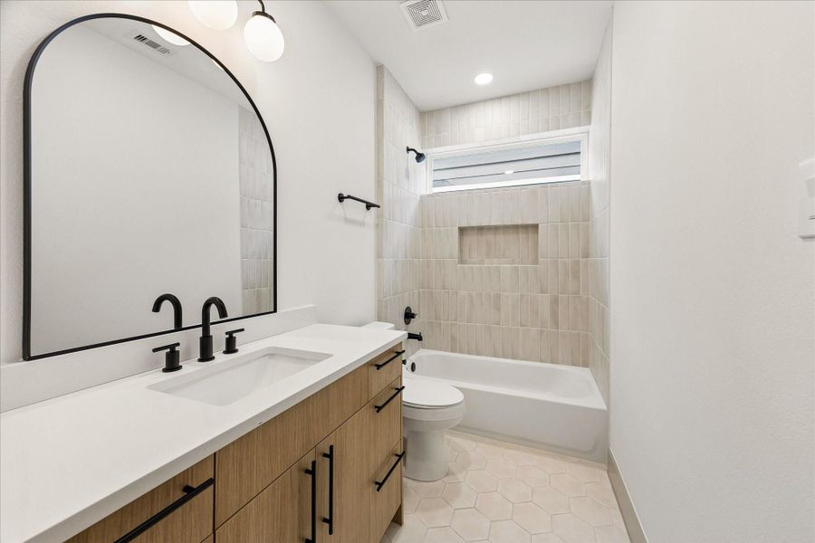 Quartz countertops, designer tile, matte black fixtures, and warm cabinetry continue the home’s cohesive design throughout every level.