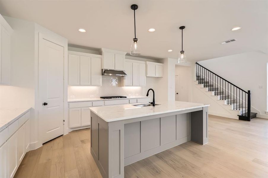 Kitchen with light hardwood / wood-style floors, white cabinetry, sink, and an island with sink