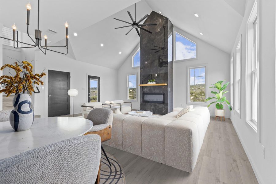Living area with a high ceiling, a tile fireplace, light wood-style flooring, a ceiling fan, and recessed lighting