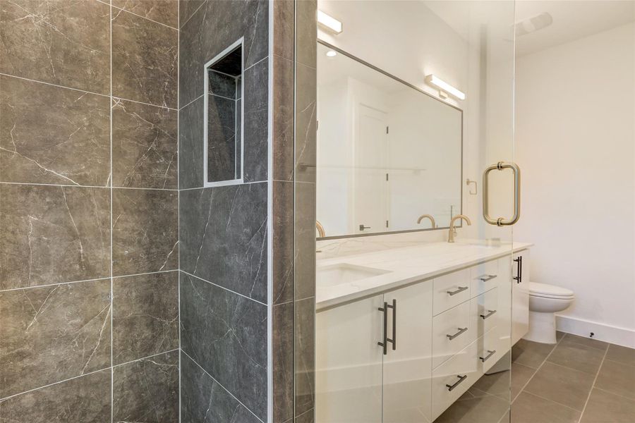 Full bathroom with toilet, double vanity, a tile shower, and tile patterned flooring